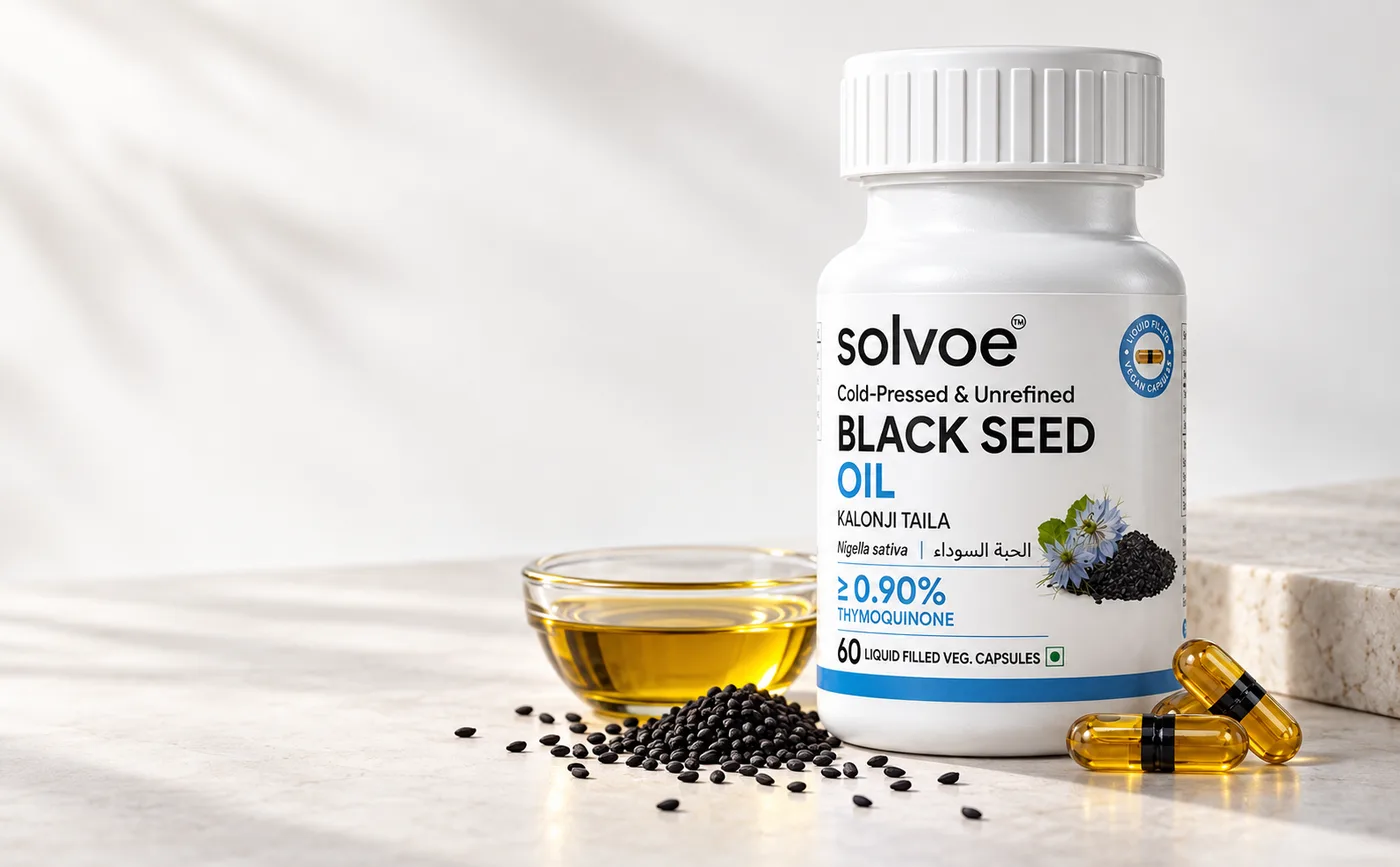 Solvoe Black Seed Oil bottle of 60 cold-pressed Nigella sativa capsules beside a glass bowl of golden black seed oil, loose kalonji seeds and three liquid-filled capsules on a stone surface